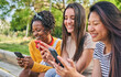 © CarlosBarquero - Three smiling young women using cell phone outdoors. Group of happy friends checking fun social networks on mobile. Cheerful classmates gossip on dating apps together. People and new technologies.