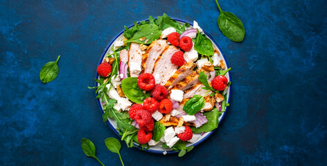 Wall Mural - Gourmet salad with raspberries, grilled chicken, feta cheese, red onion, walnuts, spinach and mixed herbs, blue table background, top view