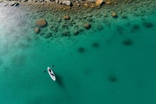 An Overhead Aerial Perspective Of A Clear Turquoise Lagoon, Where The Coral Reefs And Marine Life Beneath Are Visible. A Stand-up Paddler, Viewed Directly From Above, Casts A Minimalistic Shadow, Cont