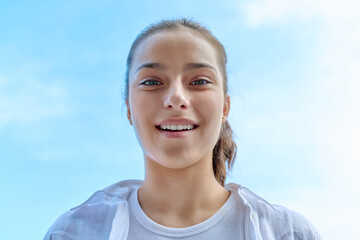 Wall Mural - Happy teenage girl smiling with rhinestone teeth looking down at camera, blue sky