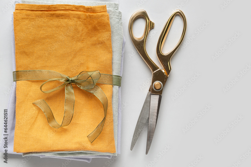 Stack of fabric tied with ribbon and scissors on light background