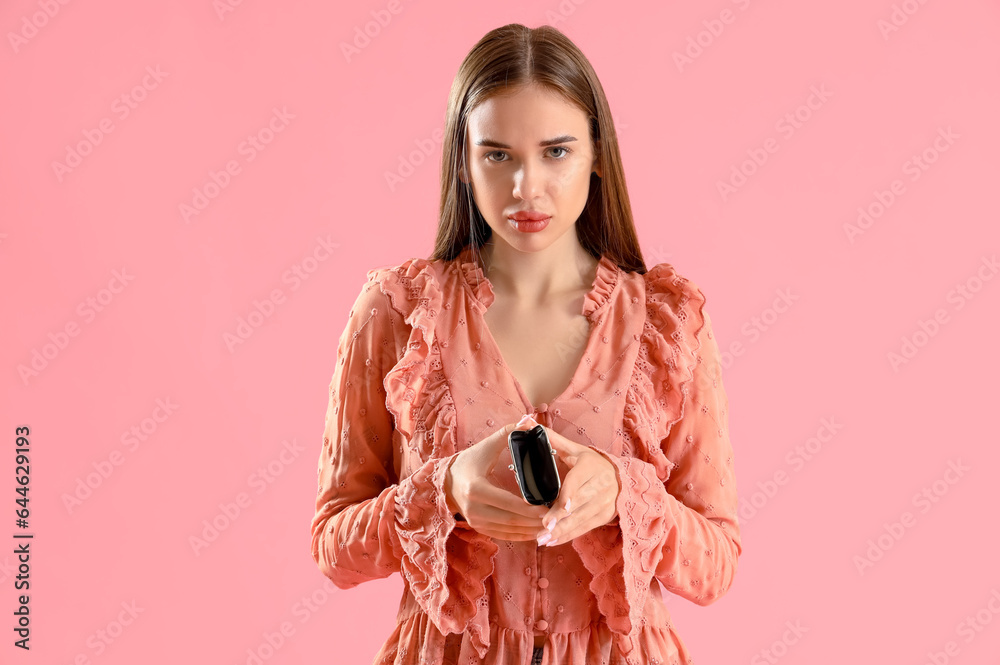 Upset young woman with empty wallet on pink background