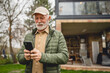© Miljan Živković - One senior man stand in front of tiny house in day use smart phone
