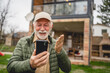 © Miljan Živković - One senior man stand in front of tiny house in day use smart phone