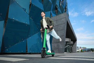 Happy man riding modern electric kick scooter on city street