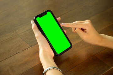 Poster - Mockup image of asian woman holding black smartphone with blank green screen on wood table.