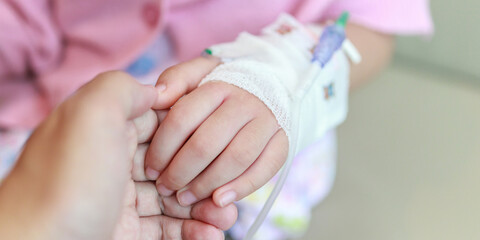 Mother holding child hand with saline IV solution in hospital