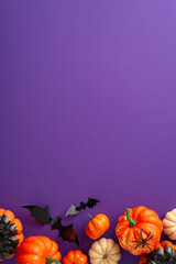 Dive into Halloween fun with this creative arrangement. Vertical top view shot of thematic decor, petite pumpkins, spectral spider, bats on violet backdrop with a blank space for greetings or ads