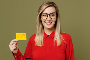 Wall Mural - Young smiling happy rich fun cool woman she wear red shirt casual clothes glasses hold in hand mock up of credit bank card isolated on plain pastel green background studio portrait. Lifestyle concept.