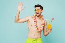 Young Man Wears Green Shorts Swimsuit Glasses Hawaiian Lei Relax Near Hotel Pool Drink Exotic Orange Citrus Cocktail Isolated On Plain Blue Cyan Background. Summer Vacation Sea Rest Sun Tan Concept.