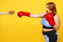 Young Chubby Overweight Plus Size Big Fat Fit Woman Wear Blue Top Red Gloves Warm Up Training Boxing Against Fast Food Burger Isolated On Plain Yellow Background Studio Home Gym Workout Sport Concept