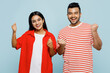 Young couple two friends family Indian man woman wear red casual clothes t-shirts together doing winner gesture celebrate clenching fists say yes isolated on pastel plain blue cyan color background.