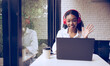 © Wosunan - Portrait of a beautiful young woman wearing headphones and smiling while using laptop in cafe, Say hello to friends in online