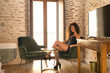 © Manuel - Young woman, beautiful, brunette, with curly hair, in a black dress, sitting in the chair of a room in a luxurious hotel, flirtatious and seductive. Concept beauty, relaxation, sensuality, seduction.