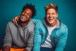 © VisualProduction - Portrait of two young male interracial best friends laughing, smiling and hugging on solid studio background.