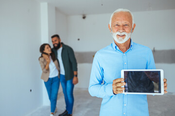 Wall Mural - Real estate agent showing new home to clients. Portrait of smiling real estate agent holding files at home. Portrait of real estate agent at his work and clients looks around apartment behind him.