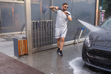 A man with a water cannon in his hand runs around the car and washes it. A car at a self service car wash.
