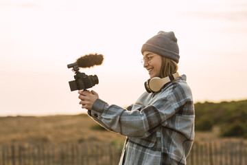 Happy lady recording vlog on camera under sundown sky