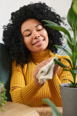 Canvas Print - Happy woman wiping leaf of beautiful potted houseplant indoors