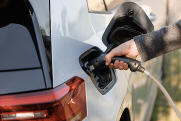 Man holding power supply cable at electric vehicle charging station. Hansome guy holding plug of the charger, while car is charging at the charging station