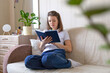 © Елена Якимова - young woman reading paper book at home on couch. education and cultural development of person. female restinng, relaxing, studying fiction, literature