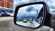 Photograph from a mobile phone in the side mirror of a car with vehicles on the road and city buildings around. The concept is journey in an urban environment, filled with traffic and urban landscape