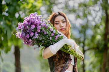 Poster - a young woman in a white dress stands on a green field and holds a large bouquet of flowers in her hands. In the background, there are forest and a lake. Lifestyle concept.