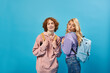 © LIGHTFIELD STUDIOS - amazed blonde teen girl looking at school backpack near cheerful redhead classmate on blue