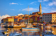 Rovinj, Croatia. Motorboats and boats on water in port of Rovigno. Medieval vintage houses of rovinj old town. Yachts landing, tower with clock. Morning sunrise in Istria with blue sky withclouds