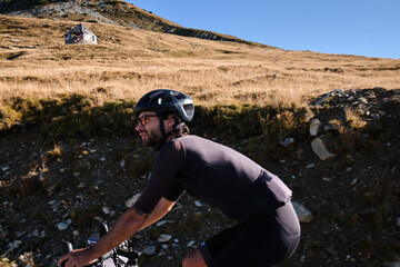 Man cyclist on a bicycle is riding on the road in the hills with a view of the mountains.Sport motivation.Cyclist wearing black cycling kit and helmet.Cyclist training on road bike.Transalpina,Romania