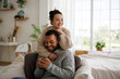 © Dmytro Hai - Smiling young asian woman in sweater hugging african american boyfriend holding coffee at home