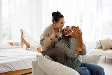 Smiling Asian Woman In Sweater Holding Coffee Near African American Boyfriend Playing With Dog At Home