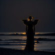 Generative KI Silhouette eines Engels mit Flügeln am Meer bei Nacht
