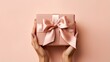 © lililia - female hands delicately presenting a kraft paper gift box adorned with a satin ribbon bow. The image is set against a soft pastel background, allowing ample space for adding a personalized message.