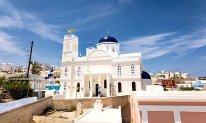 Santorini, Greece - 05 25 2023: Greek orthodox church in Karterádos in the traditional white color and a blue dome with clouds in the background