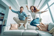 © VisualProduction - Beautiful young energetic caucasian couple jumping off sofa in the living room and smiling, young love