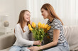 © New Africa - Daughter congratulating mom with bouquet of yellow tulips at home