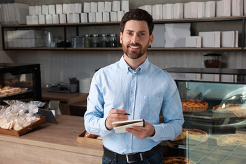 Wall Mural - Happy business owner with notebook and pen in bakery shop