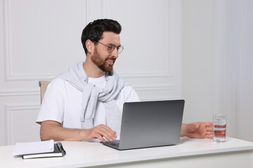 Canvas Print - Man with laptop and glass of water at white table indoors