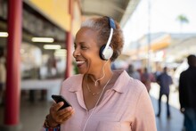 Portrait Of Happy African American Woman Listening To Music With Mobile Phone At Train Station