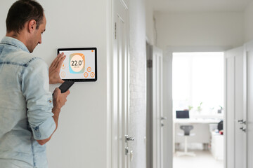 Poster - Young man controlling temperature in the living room with smart phone and digital touch screen panel. Concept of heating control in a smart home
