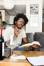 Vintage Photo Of A Young Afro Boy Reading A Book And Smoking On The Sofa At Home. Vertical Photo