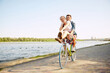 © Lustre Art Group  - Young cheerful, lovely couple enjoying, having fun, rejoice cycle ride over river embankment in hot summer day.