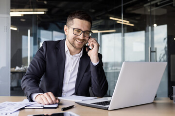 Smiling young man lawyer, notary works in the office at the laptop, talks and consults on the phone with clients