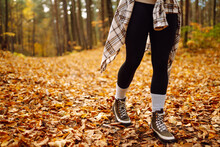 Woman's Legs In Boots In Autumn Foliage. Leaf Fall. A Woman Tourist Walks Through Fallen Leaves In The Autumn Forest. Lifestyle Concept.