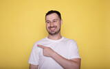 Fototapeta Do przedpokoju - Photo of brunet hair smiling man directing finger mockup new supermarket promo isolated on yellow background.