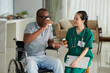 © DragonImages - Sick patient in wheelchair taking pills and drinking water