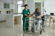 © DragonImages - Social worker helping patient to stand up from wheelchair leaning on walkers