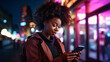 © TimeaPeter - Nightlife in big city. Beautiful african american woman holding her phone with neon city lights in the background.