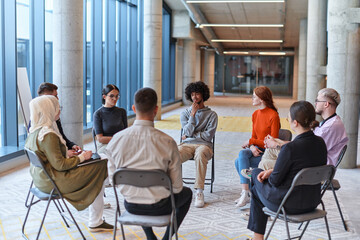 A diverse group of young business entrepreneurs gathered in a circle for a meeting, discussing corporate challenges and innovative solutions within the modern confines of a large corporation